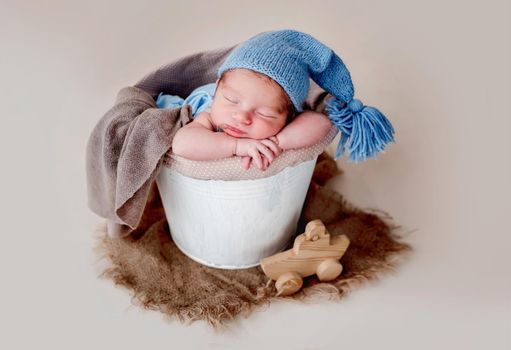 Funny newborn wearing blue knitted hat and resting in busket