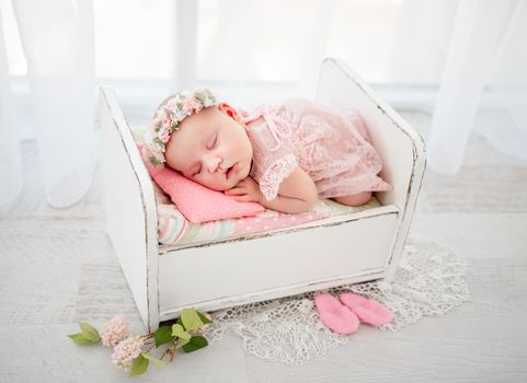 Newborn baby girl wearing cute costume sleeping in the little designed bed and holding her hands under cheek. Beautiful infant child napping lying on her tummy. Pretty kid resting in light room