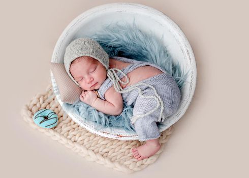 Cute newborn sleeping in round cradle beside knitted donut
