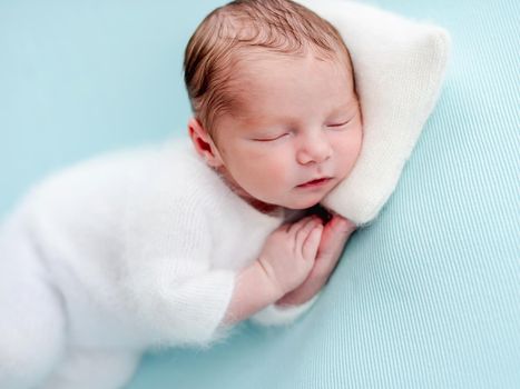 Lovely newborn in white clothes resting with head on tiny pillow