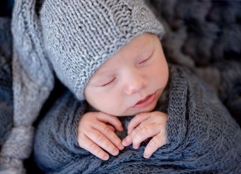 Charming newborn in gray hat wrapped in shawl