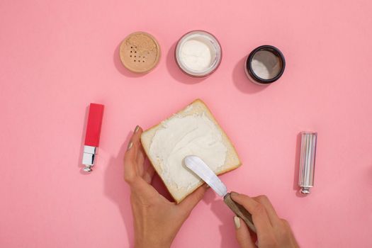 Female hands smear cosmetic cream on a piece of bread for a truck next to cosmetics and jars of supplies