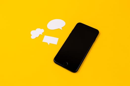Smartphones with paper speech bubbles on yellow background. Communication concept. Top view. Copy space. Paper composition