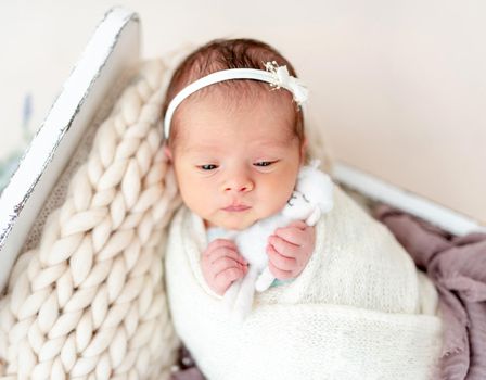 Adorable awake newborn in white diadem