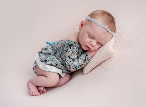 Newborn girl wearing diadem and dress resting on tiny pillow