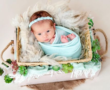 Sweet newborn with open eyes lying in cradle
