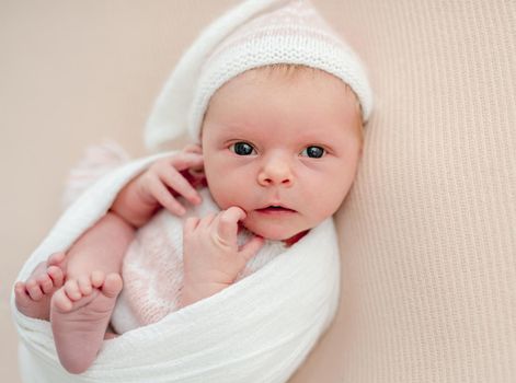 Sleepless newborn in white suit and hat lying calmly