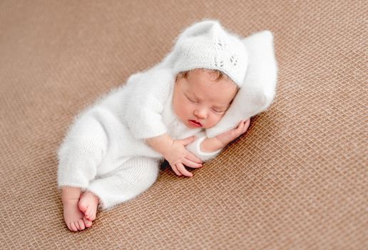 Cute newborn in white suit resting on tiny pillow