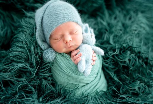 Lovely newborn in green knitted hat wrapped in blanket