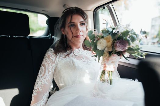 Wedding photo of the bride who is sitting in the car with a bouquet of flowers