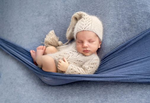 Adorable newborn baby boy wearing cute knitted hat and costume sleeping during studio photoshoot. Infant child napping