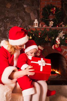 Mother and son are sitting near fireplace and christmas tree. Family look into a gift box.