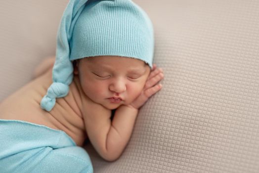 Newborn in blue hat and pants sleeping lying on stomach