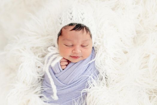 Smiling newborn in knitted hat on white fluffy blanket