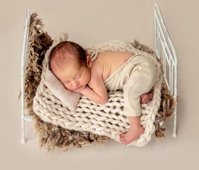 Funny newborn sleeping on tiny bed with pillow