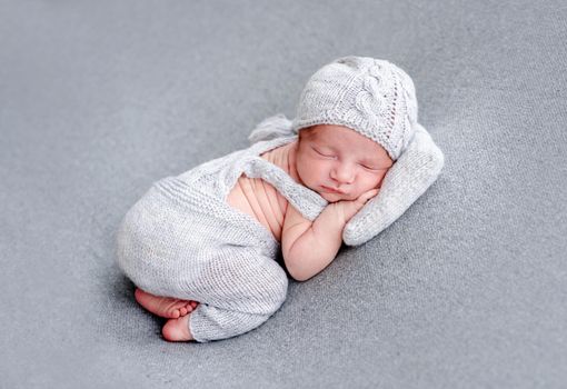 Charming newborn in knitted gray suit sleeping on tiny pillow