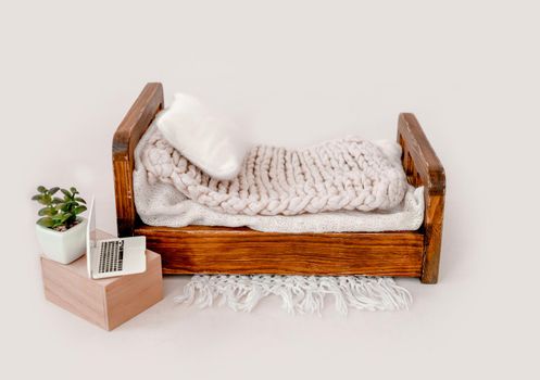 Wooden bed decor for newborn studio photoshoot with knitted blanket and pillow closeup. Infant baby photo furniture and toy laptop