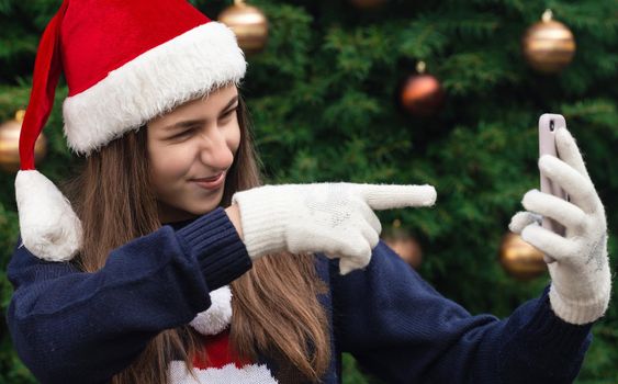 Christmas online greetings. girl in santa claus hat talks and using mobile smartphone for video call friends and parents. Christmas during coronavirus.