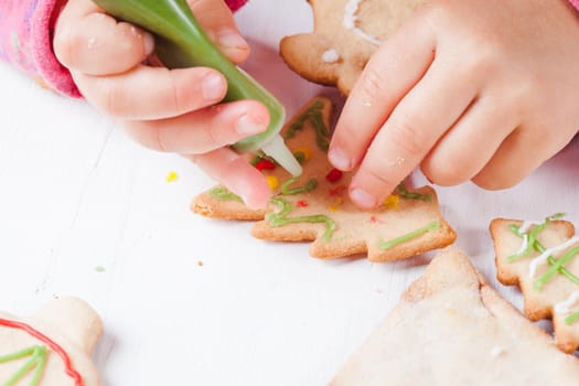 Hands of little girl, who draws on gingerbread cookies