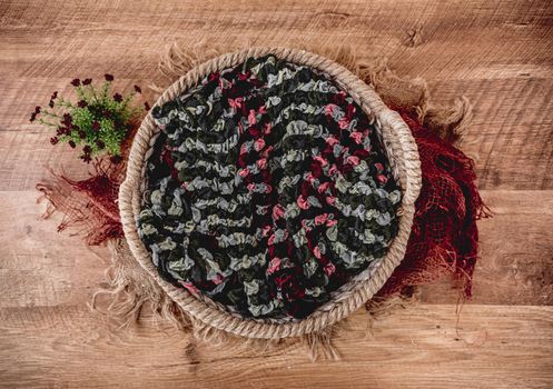 Beautiful background for newborn photosession with plants. Digital composite with knitted basket filled with colorful fabric and standing on sackcloth