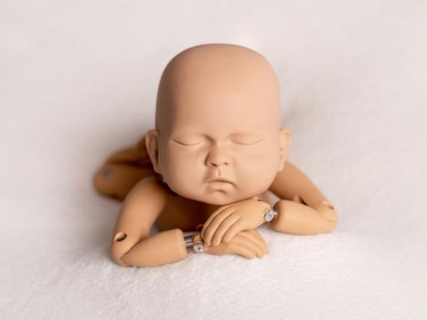 Realistic plastic figure of newborn child for photographing practice, with head on hands, isolated on white background