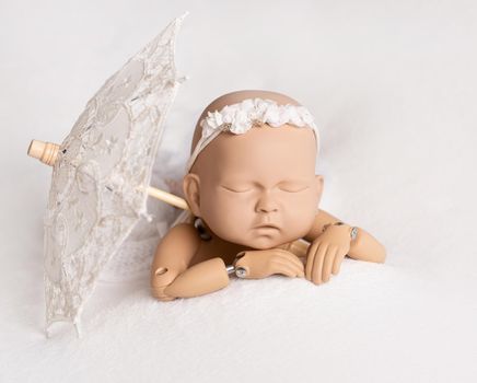Similar to alive, doll of newborn kid laying on bed with headband and sun umbrella, isolated on white