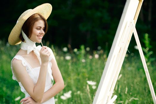 Woman in white dress in nature paints a picture of a landscape hobby. High quality photo