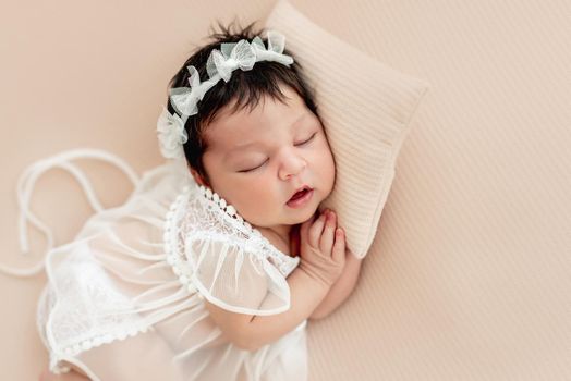 Cute newborn in lace dress sleeping on side with tiny pillow