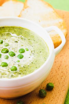 Fresh peas cream soup in a bowl on a wooden board and croutons