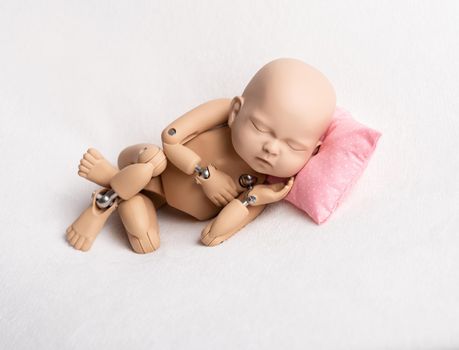 Accurate doll of newborn baby on pink pillow for photo practicing, on white background