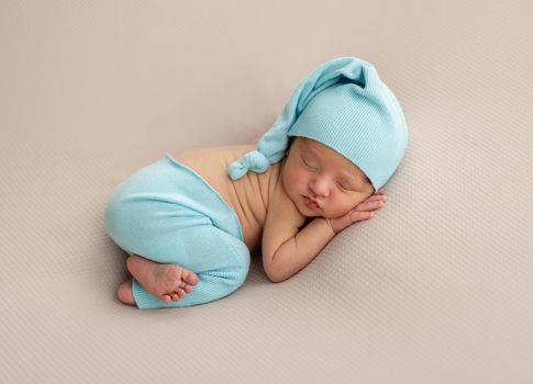Newborn in blue hat and pants sleeping lying on stomach