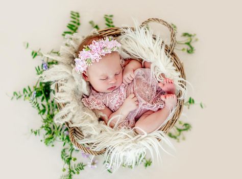 Sleeping newborn baby girl in a pink dress in a basket with flowers