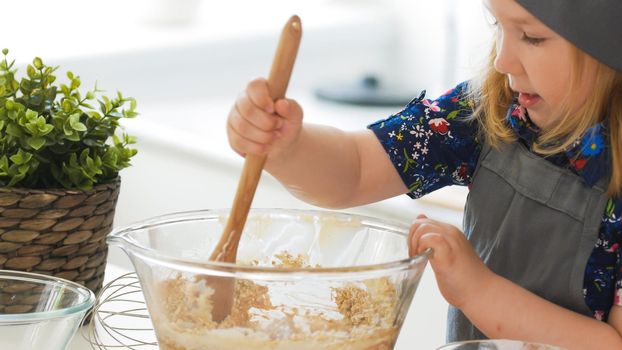 Girl baker mixes the mixture for cookies with a whisk, close up