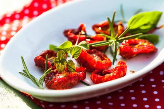 sun dried tomatoes on a white plate with fresh herbs - rosemary, basil and oregano