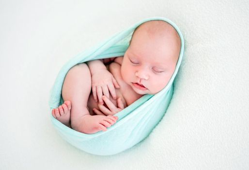 Adorable newborn baby girl lying on her back in the cocoon on white background and sleeping. Sweet infant child napping during studio photoshoot