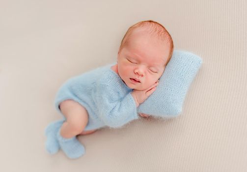 Newborn baby boy wearing knitted costume and socks sleeping on pillow and holding tiny hands under his cheeks. Adorable infant child napping