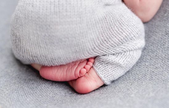 Bare feet of newborn wearing knitted gray suit