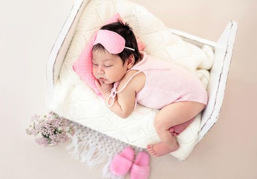 Charming newborn with pink sleep mask lying on tiny bed