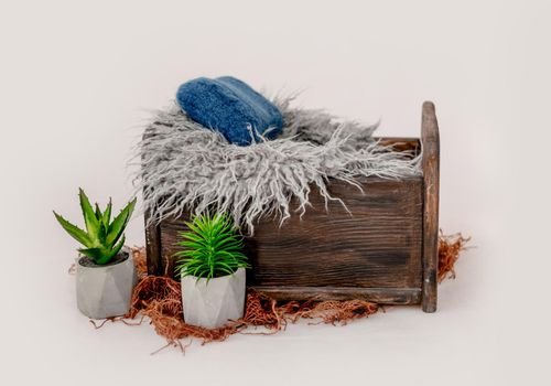 Wooden bed decor for newborn studio photoshoot with fur and knitted pillow closeup. Infant baby photo furniture and plants