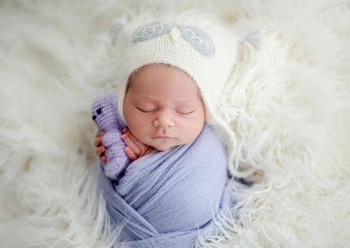 Newborn sleeping with knitted toy in tiny hands