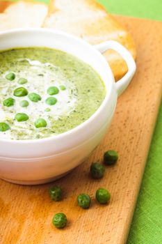 Fresh peas cream soup in a bowl on a wooden board and croutons