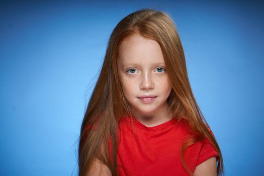 cute red-haired girl in red t-shirt emotions blue background. High quality photo