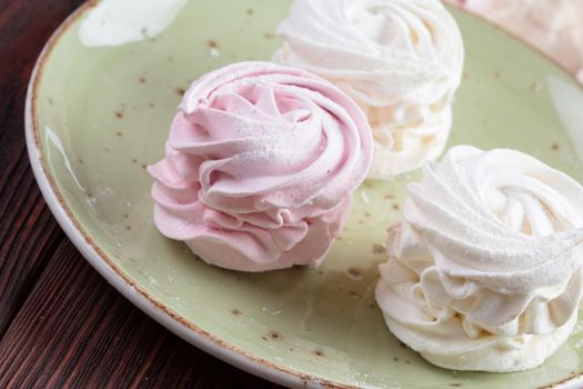 Pink and white meringue cookies on green plate close up