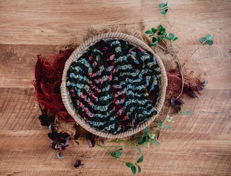 Beautiful background for newborn photosession with plants. Digital composite with knitted basket filled with colorful fabric and standing on sackcloth