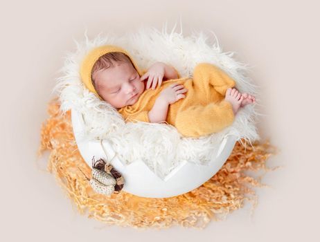 Cute newborn in yellow knitted suit lying in egg cradle