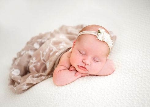 Newborn baby girl wearing beige dress sleeping and holding her hands under cheek. Little cute infant child napping lying on her tummy. Adorable kid during studio photoshoot