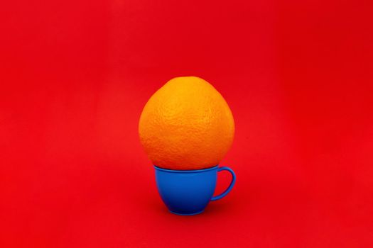 Round orange on small blue plastic mug on red background. Minimalism. Enough space for text.