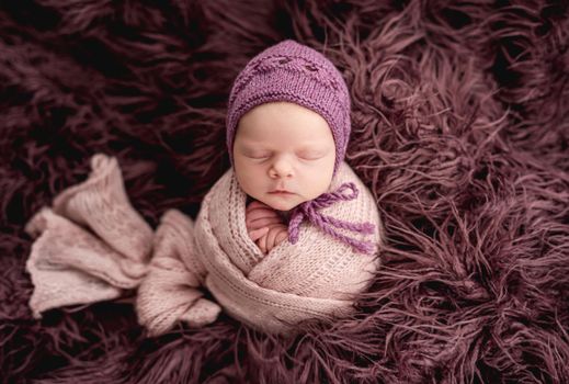 Newborn wrapped in knitted blanket wearing handmade hat