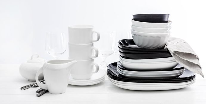 Stack of black and white plates, mugs and glasses on white surface