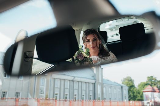 The reflection of the bride in the rearview mirror of the car.